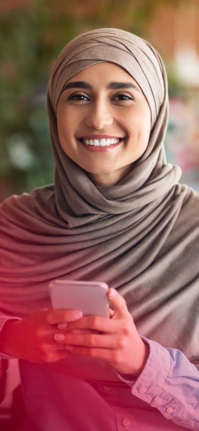 A smiling learner holding her phone, from the IELTS brand photography washed in the brand's red gradient